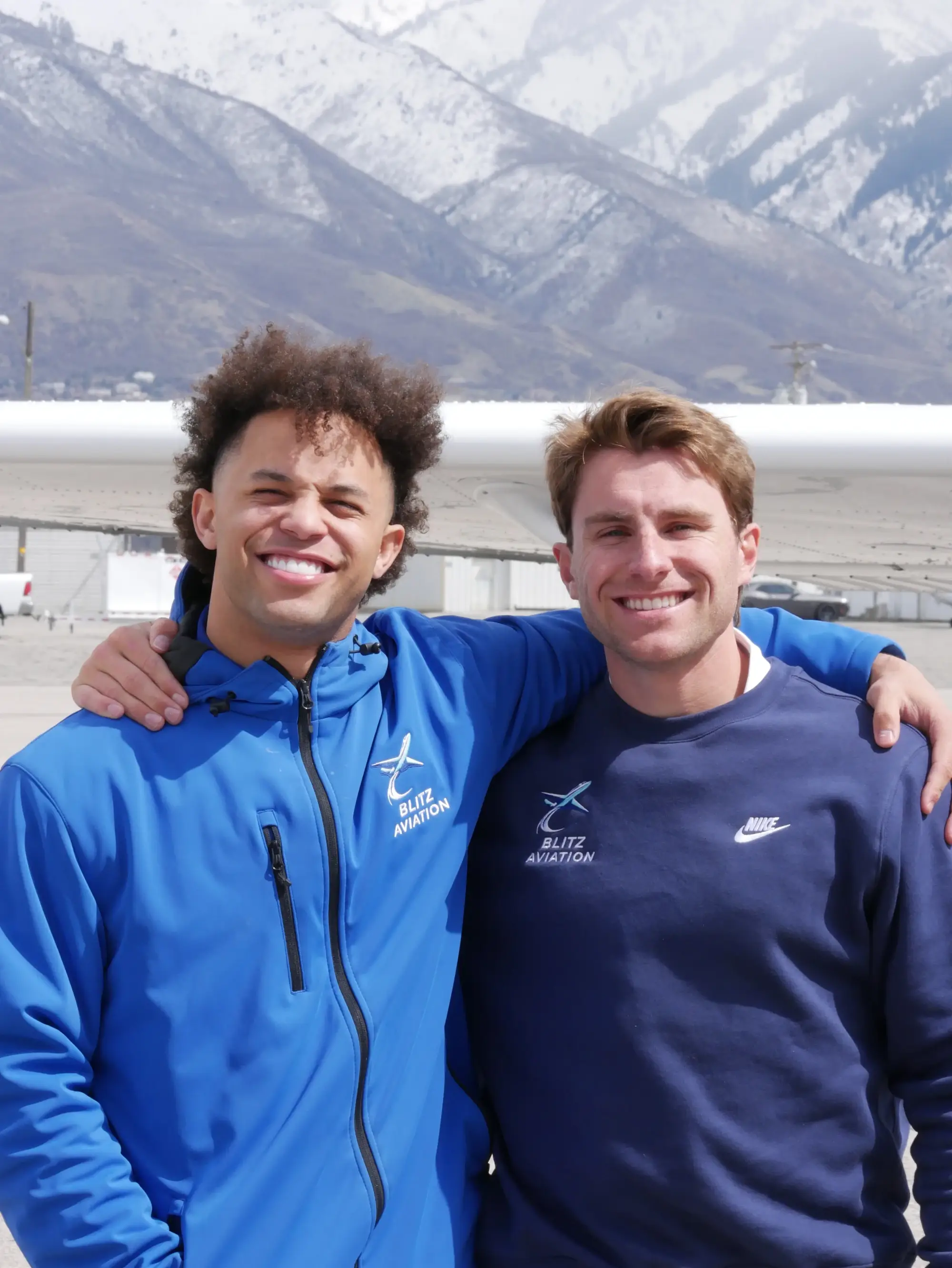 Two man smiling while looking at the camera during daytime with mountains in the background