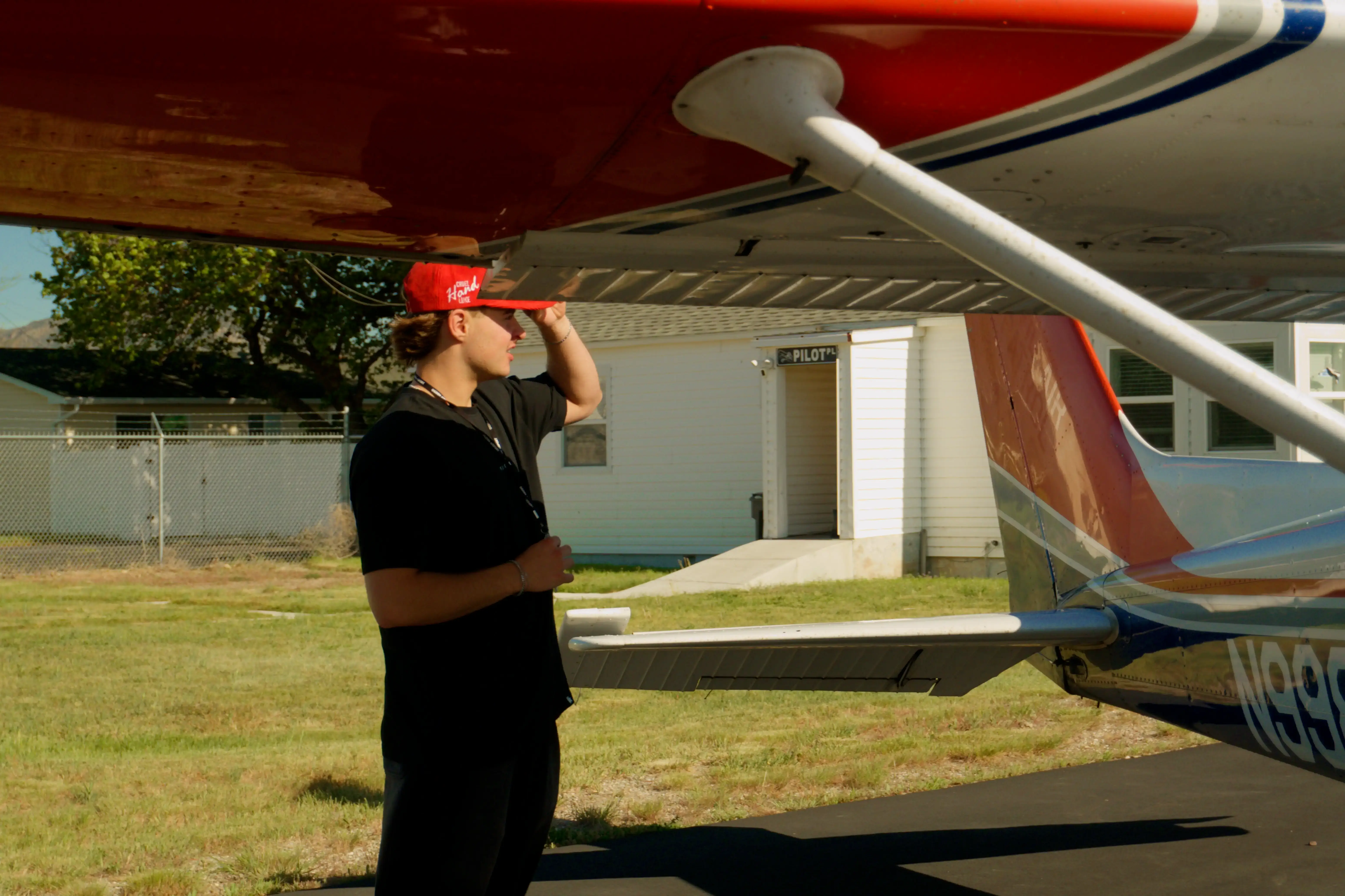 Student pilot in a red cap checking the wing and tail of a Cessna 172P during a preflight walk-around