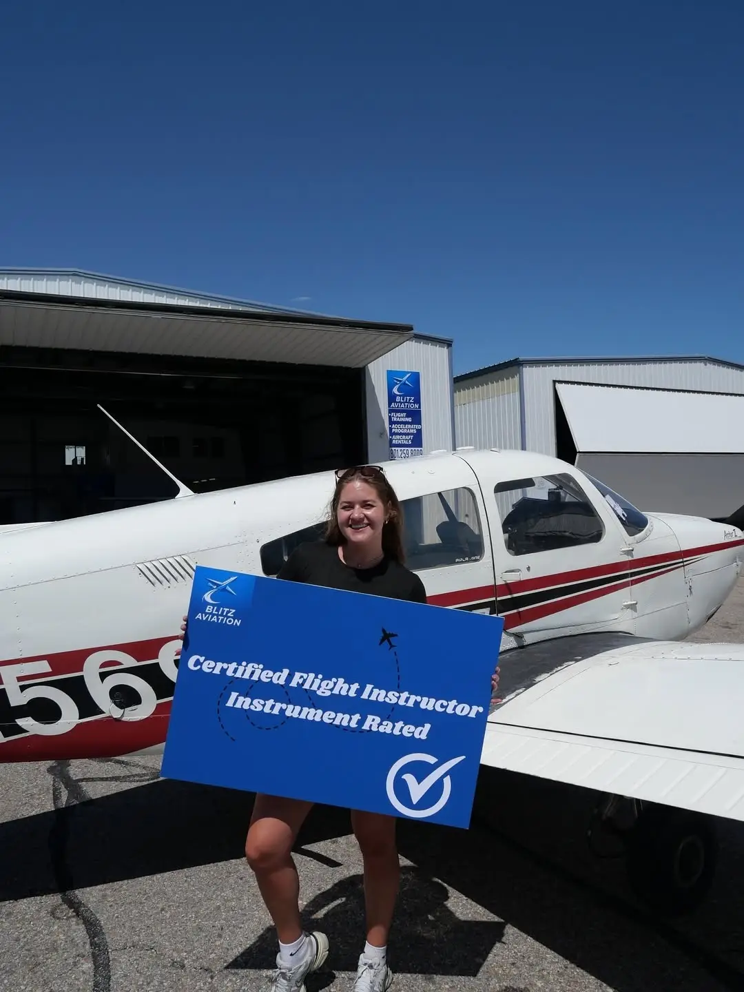 Student in front of an airplane holding a poster with "Certified Flight Instructor Instrument Rated" written on it