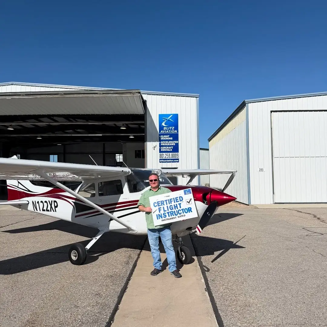 Student in front of an airplane while holding a poster with "Certified Flight Instructor Instrument Rated" on it