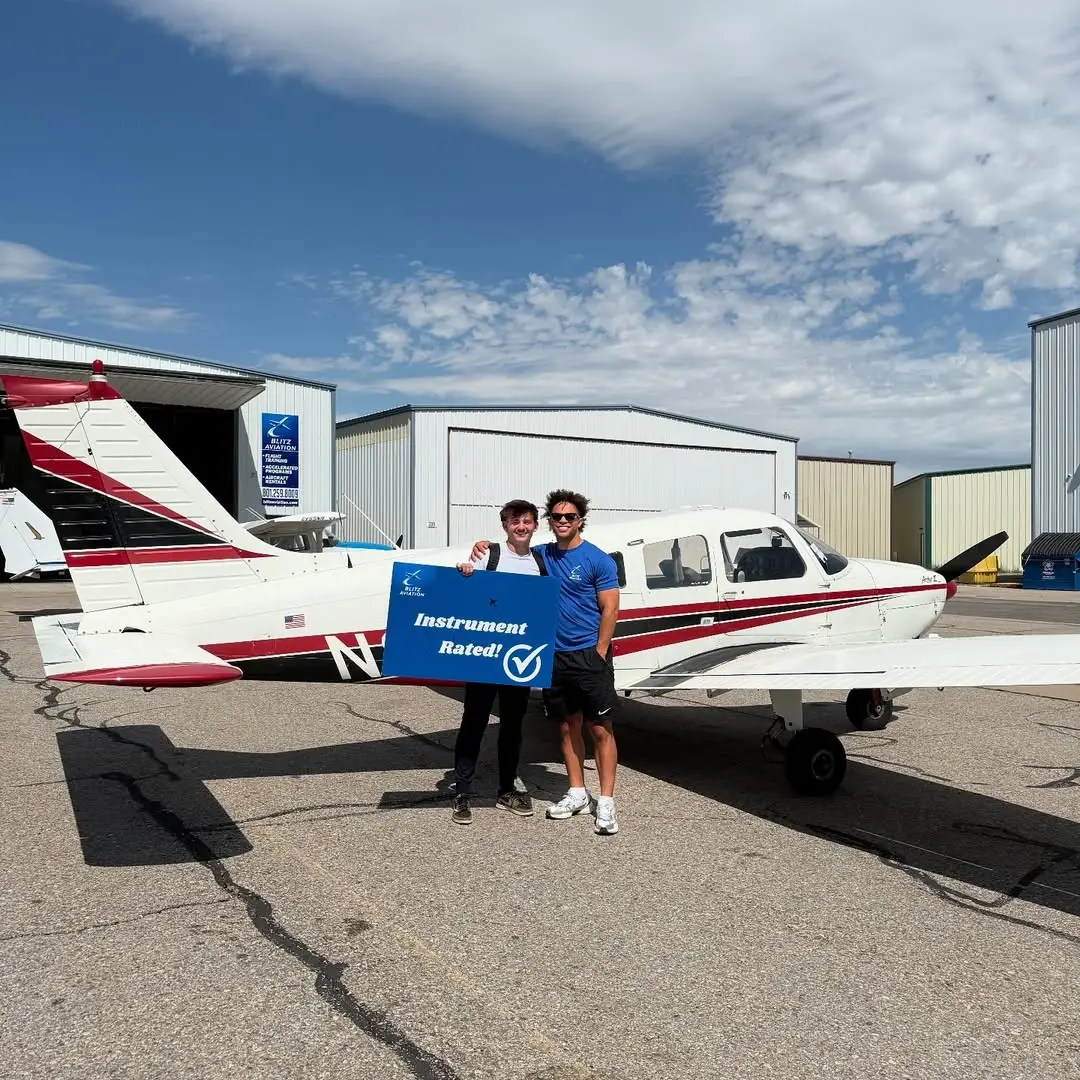 Student and CFI standing in front of an airplane while holding a poster with "Instrument Rated" written on it