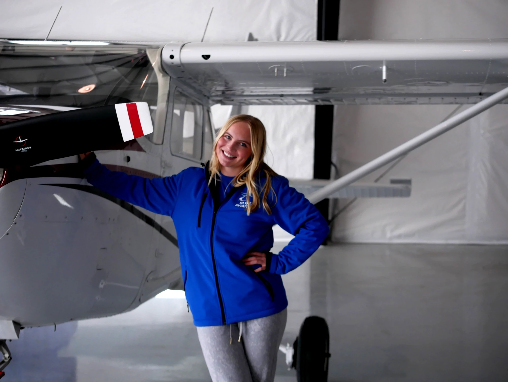 Woman smiling in front of an airplane during daytime with mountains in the background